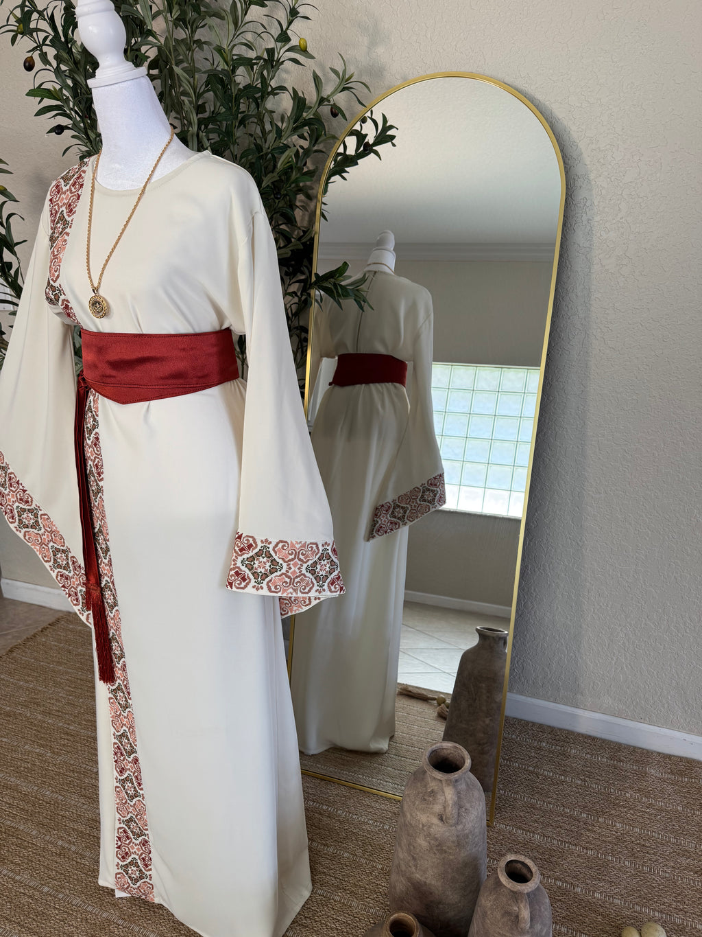 The Andalusian Abaya displayed on a mannequin features intricate embroidered trim along the front and sleeves, paired with a wide deep red sash, embodying elegant modest fashion with a luxury embroidered abaya style.