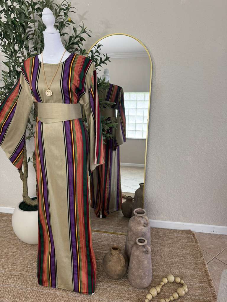 The Desert Bloom Abaya displayed on a mannequin features vibrant vertical stripes in warm tones with a wide sash belt, styled in an elegant, modest fashion setting.