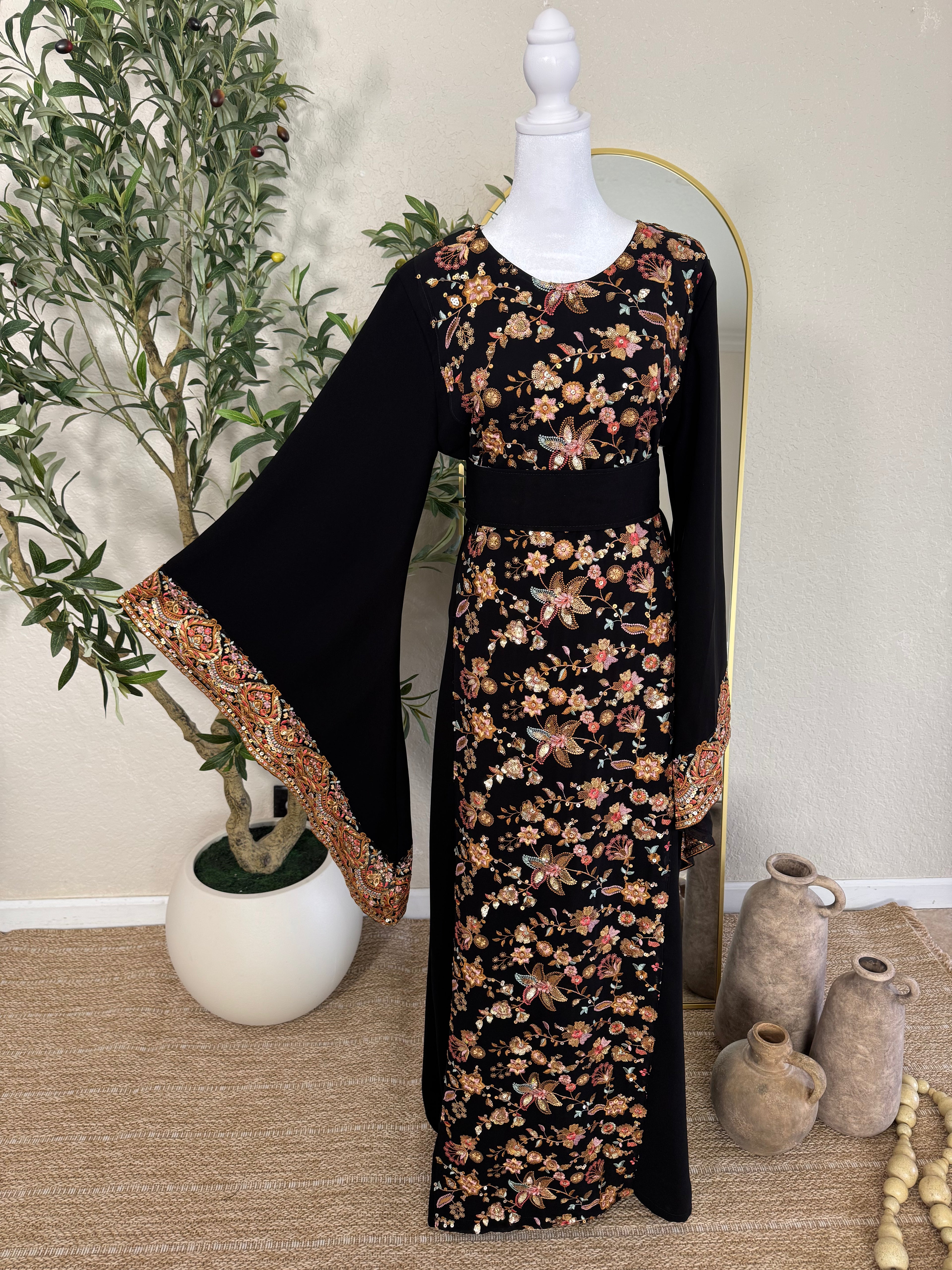 The Midnight Garden Abaya featuring intricate floral embroidery in warm tones on a black base with wide bell sleeves and detailed cuffs, displayed on a mannequin.