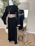Mannequin dressed in The Olive Nights Abaya, a black modest dress featuring colorful striped detailing on the waistband, sleeves, and hem, styled with a gold pendant necklace.