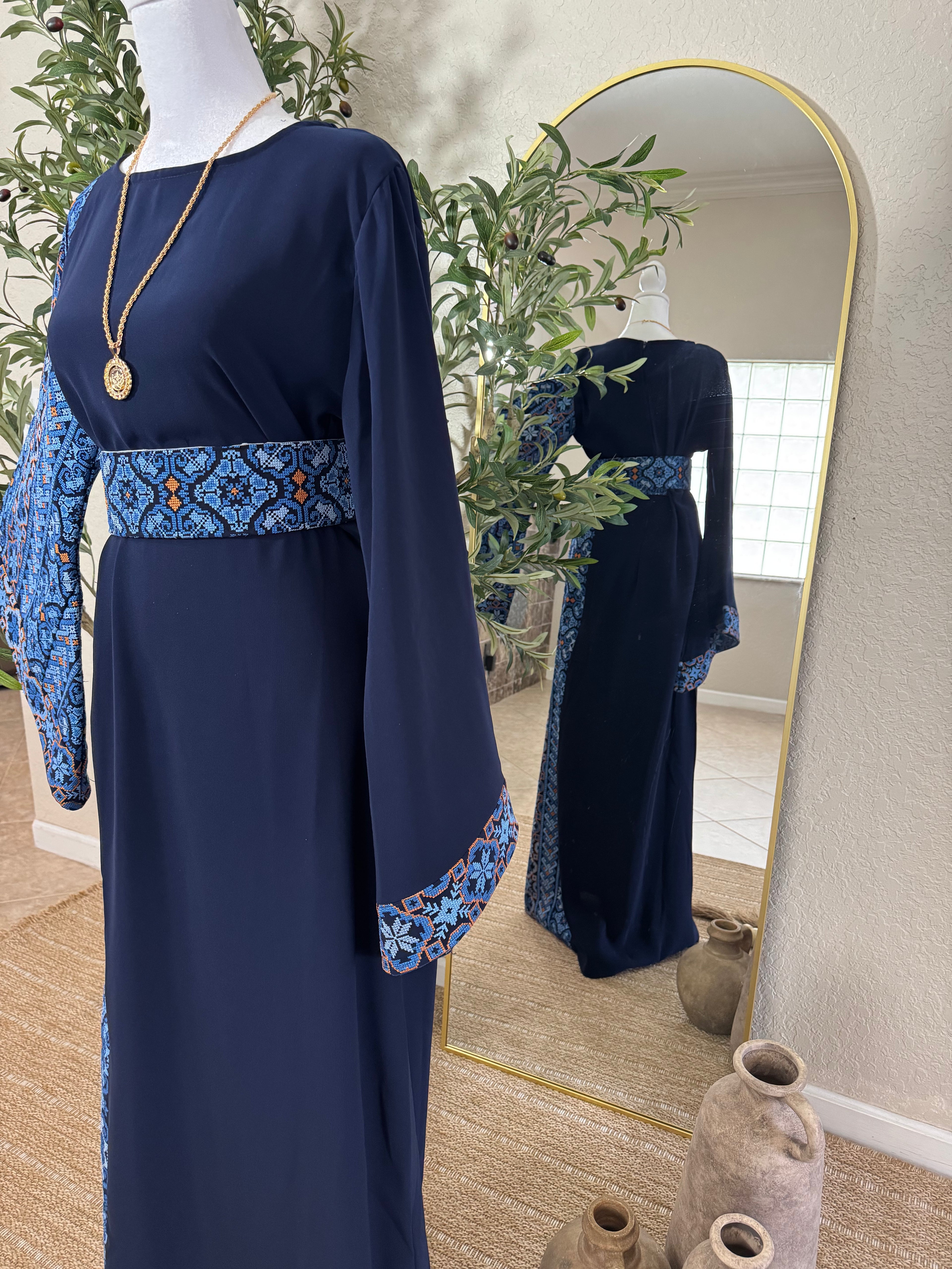 The Sapphire Thoub displayed on a mannequin features a deep navy blue fabric with intricate blue and orange embroidered patterns on the belt, sleeves, and side panel, showcasing elegant and modest fashion.
