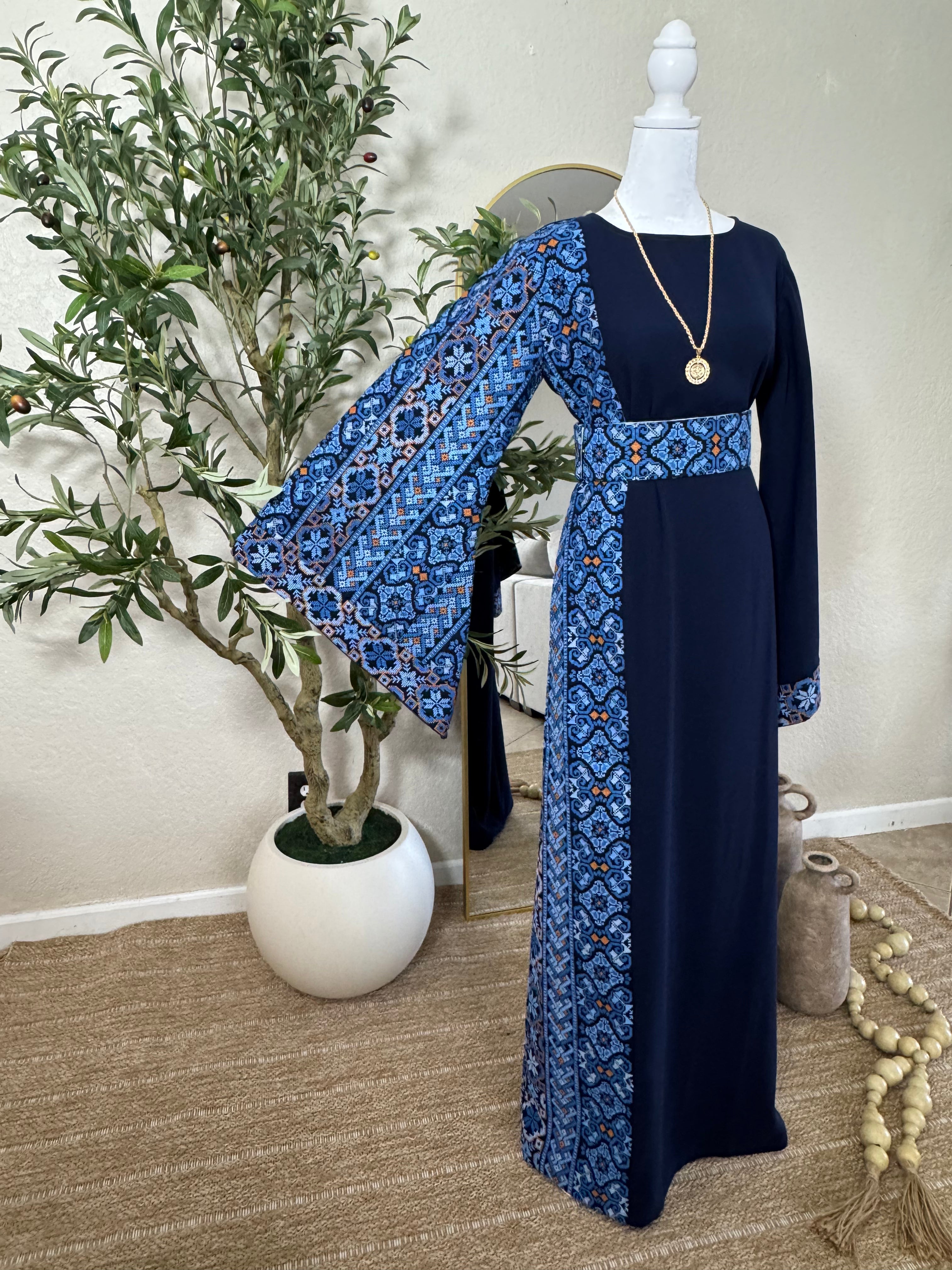 The Sapphire Thoub displayed on a mannequin features elegant blue and black embroidered patterns on the sleeve, waist, and side panels, showcasing luxury modest fashion with traditional Palestinian design elements.