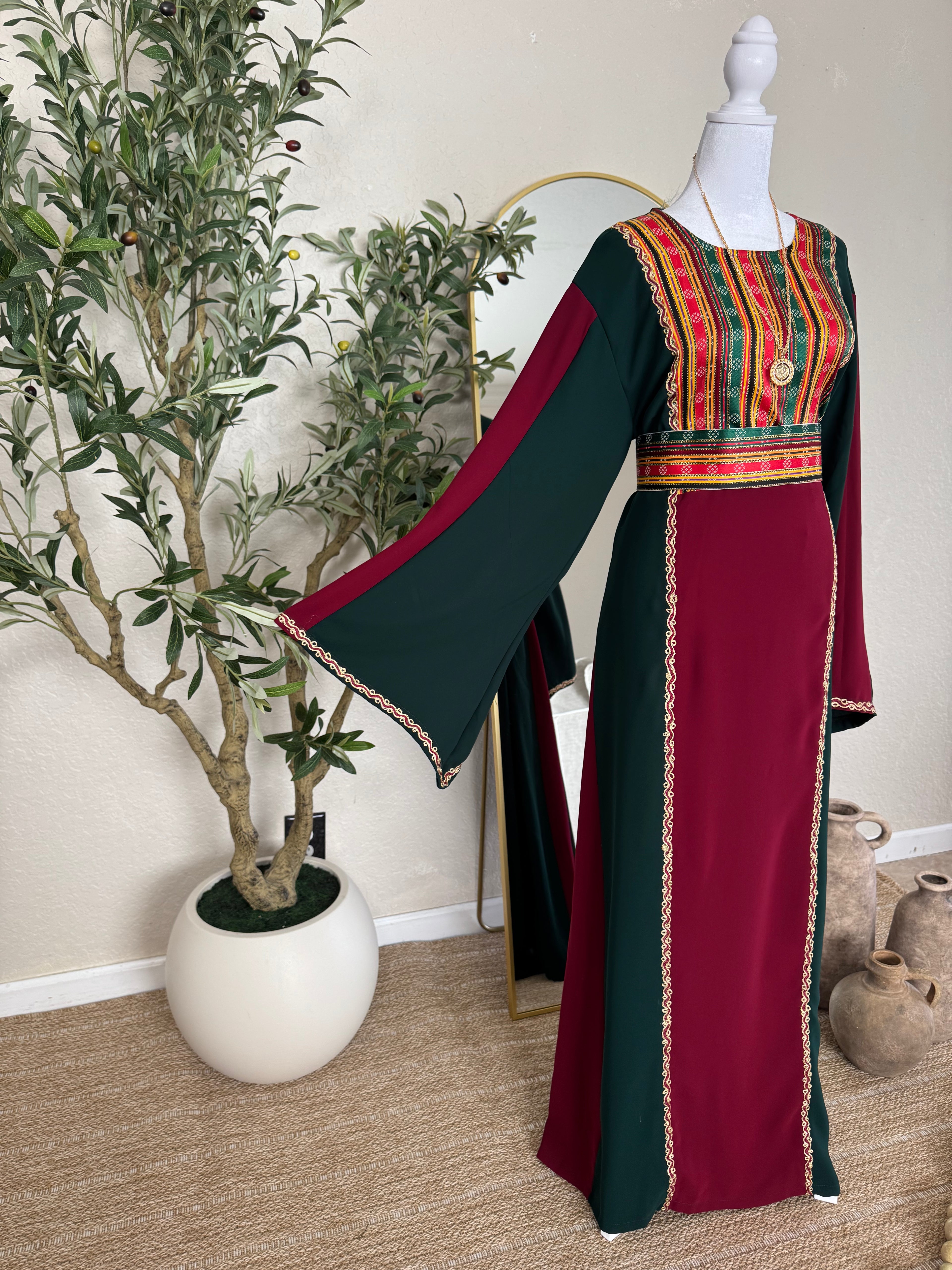 The Sultana Thoub displayed on a mannequin, featuring a rich burgundy and dark green color palette with intricate traditional Palestinian embroidery on the bodice and sleeves, embodying elegant modest fashion.