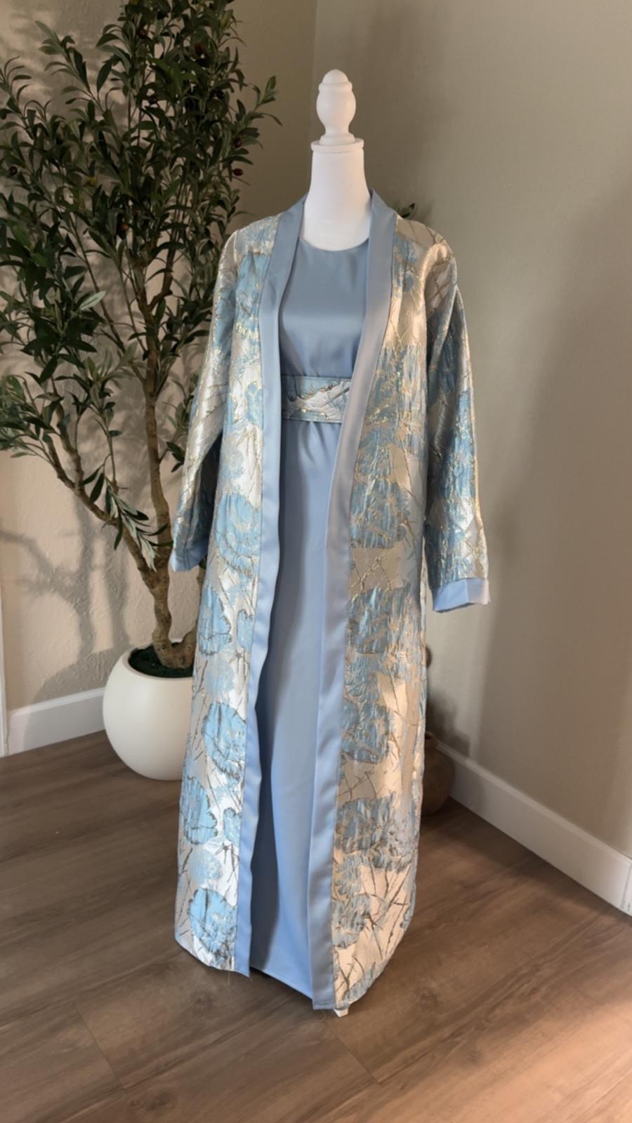 Angled front view of The Azure Bloom Abaya featuring metallic silver and blue floral fabric with powder blue satin trim