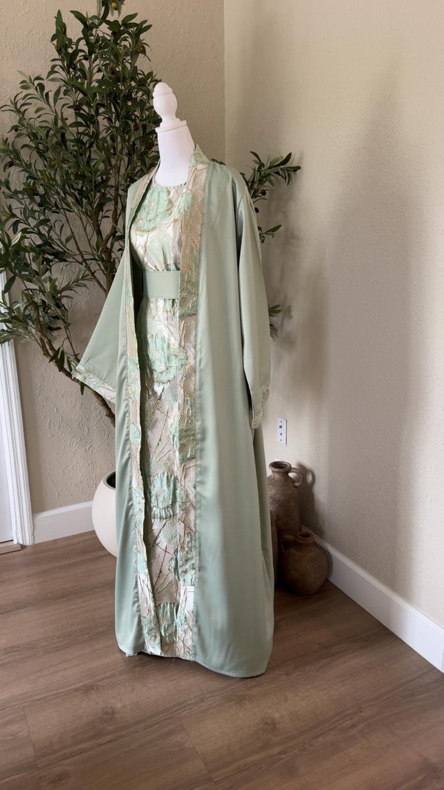 Angled view of Mint Pearl Palestinian abaya with sage green fabric and floral center panel, made in Palestine
