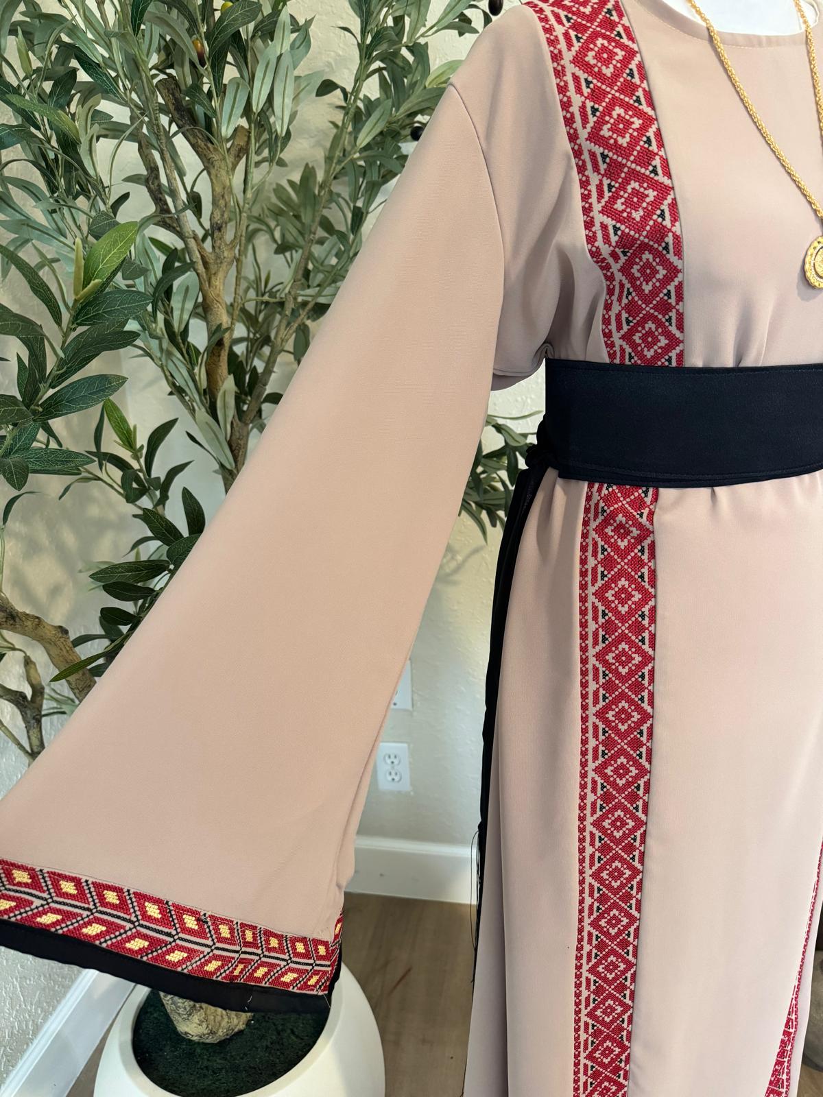 Close-up of The Ramallah Line Abaya showing red geometric front bands, patterned sleeve trim and black waist belt