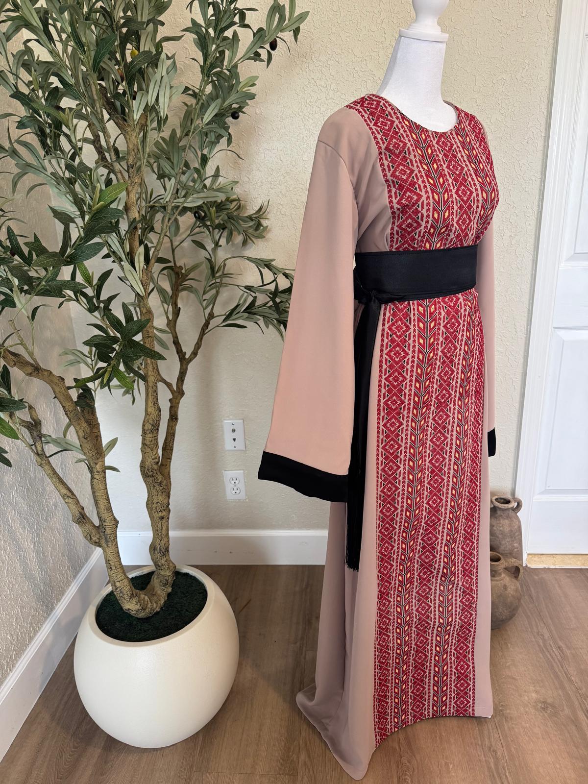 Front angled view of The Ramallah Ruby Palestinian Abaya with red geometric patterned panel, dusty taupe fabric and black belt