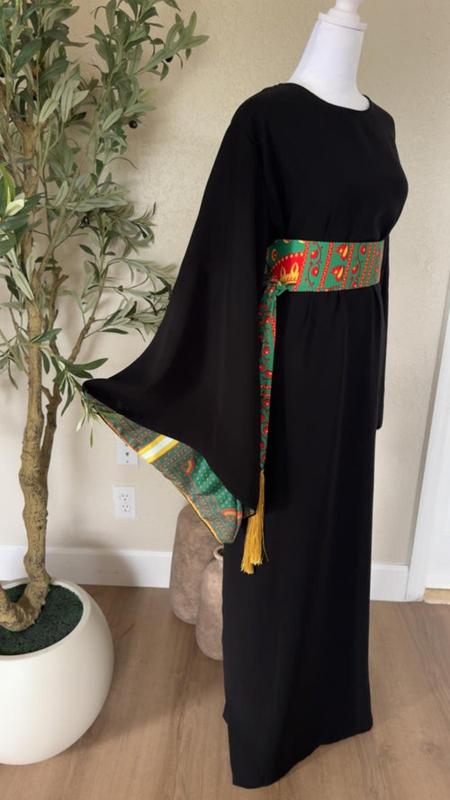 Side view of The Asba Sash Dress in black with patterned waist sash and golden tassel detailing