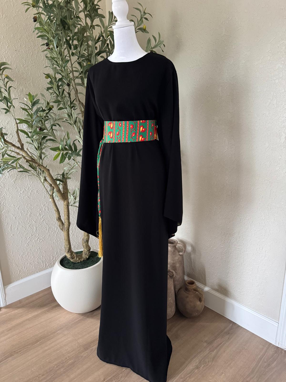 Full front view of The Asba Sash Dress in black with colorful patterned sash and golden tassels
