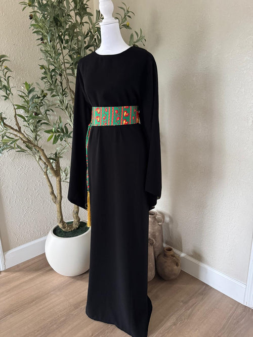 Full front view of The Asba Sash Dress in black with colorful patterned sash and golden tassels