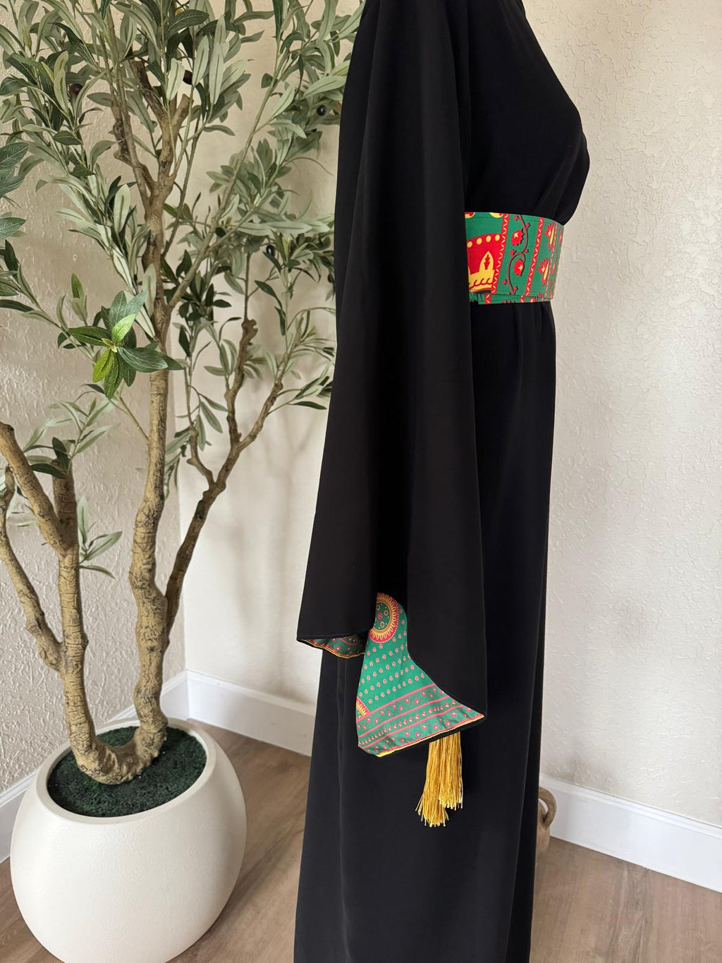 Side view of The Asba Sash Dress in black with patterned waist sash and golden tassel detailing