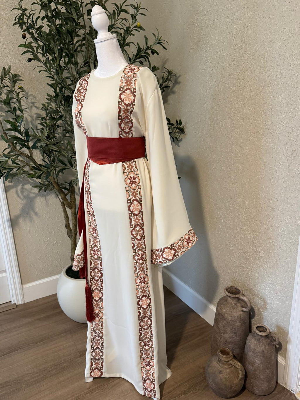 Close-up of The: Bethlehem Sand Thobe featuring an ivory base, terracotta heritage-inspired trim, wide sleeve and rust-red waist belt