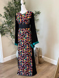 Full-length view of The: Jaffa Garden Thobe featuring a black silhouette, vibrant multicolor floral front panel, turquoise cuffs and black waist belt